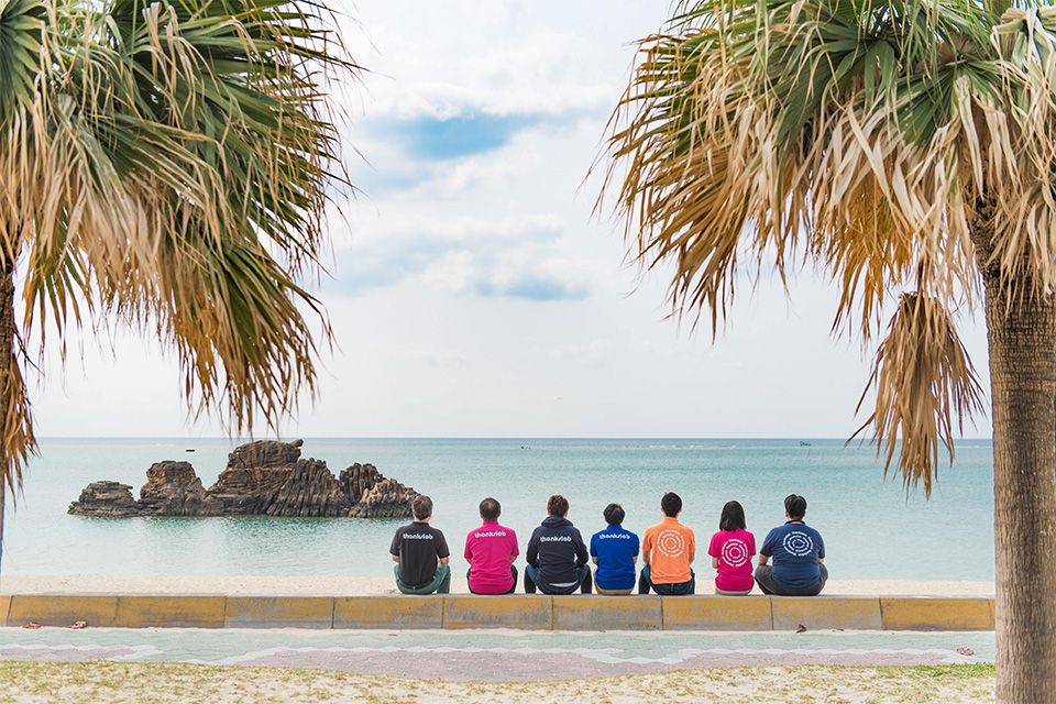 沖縄の海にむかって座るサンクスラボの社員たち