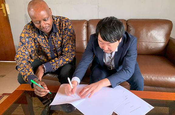 ソファーに座りスーツ姿で書類に署名するサンクスラボの社員と、それをみるルワンダの人