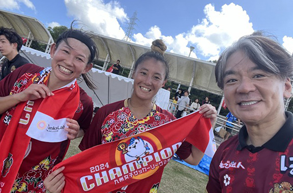 琉球FCさくらの選手2名と代表（赤いユニフォームとタオルを着用）