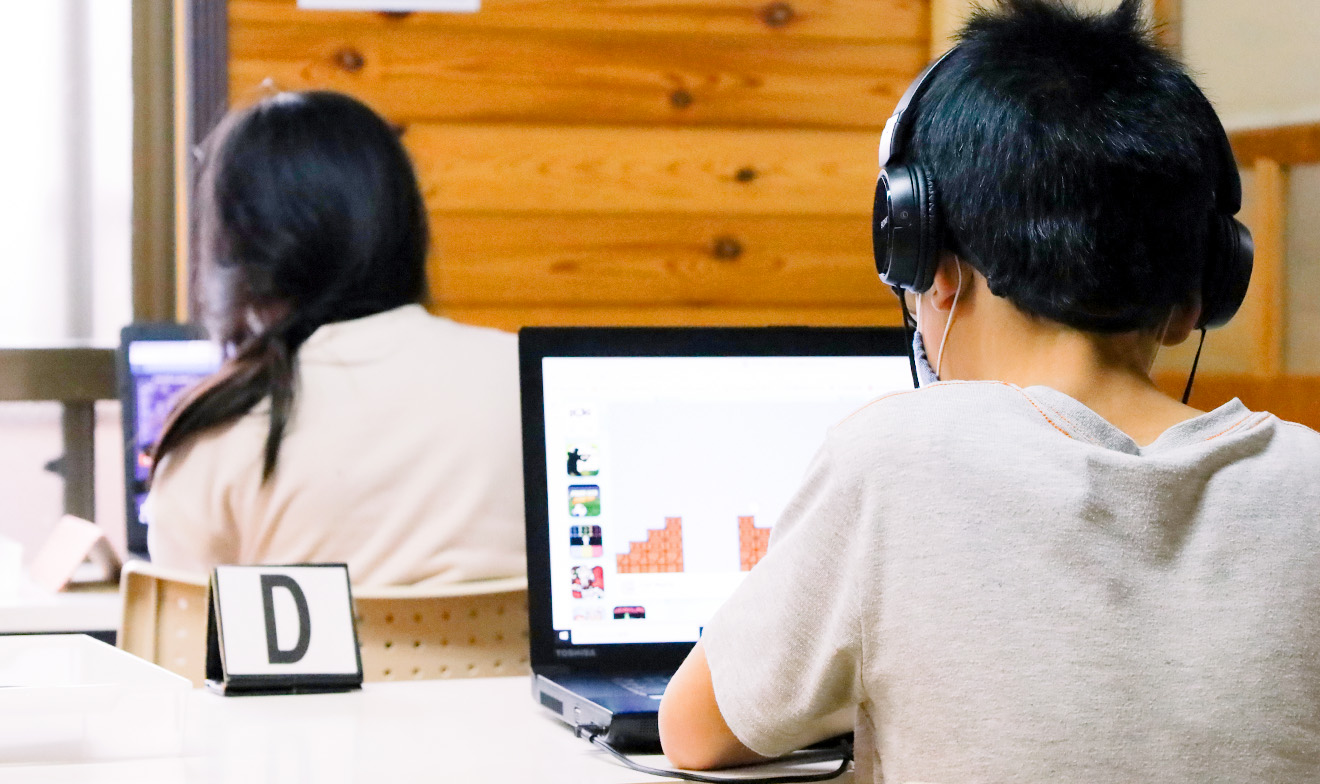 室内でノートパソコンを操作する子供たちの背中